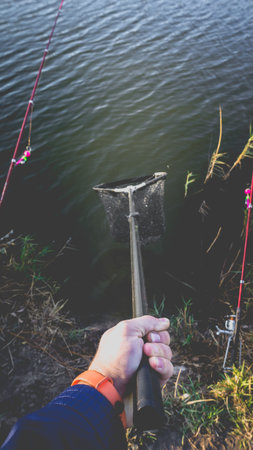 Landing net in a man's hand against the background of the lake. Photo toned with vignetting.