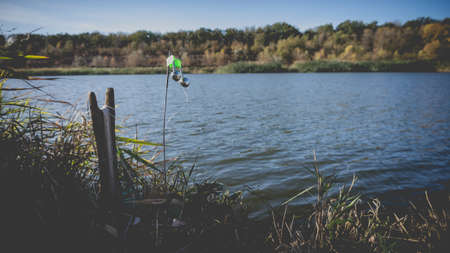 Fishing bottom tackle with green bell on the lake shore in autumn. Toned photo with the vignetting.の写真素材