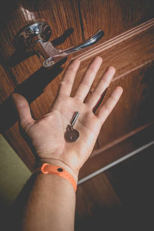 A man holds in his hand a small light broken key against the background of a door lock. Photo in the old style with vignetting.の写真素材