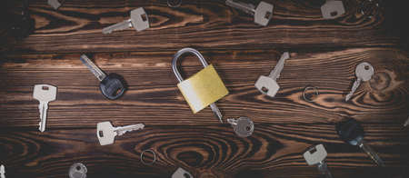 Studio photo of a lock with a broken key in it on a wooden background. Lots of other new keys around the lock. Photo in the old style with vignetting.の写真素材