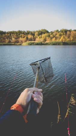 Landing net in a man's hand against the background of the lake. Photo toned with vignetting.