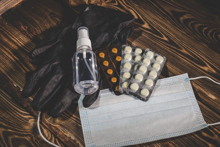 Medical mask, pills, antiseptic in a transparent plastic bottle and black rubber gloves on a wooden background. Covid-19 virus protection medical concept. Studio photo with vignetting.の写真素材