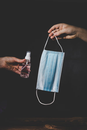 Children's hands hold a sanitizer and a blue medical mask on a black background.の写真素材
