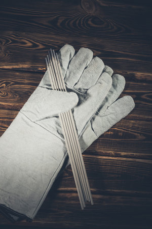White leather welding glove and welding electrodes on a wooden background. Studio photo in hard...