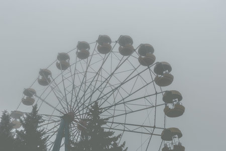 Ferris wheel in an old abandoned park in the autumn in thick fog.