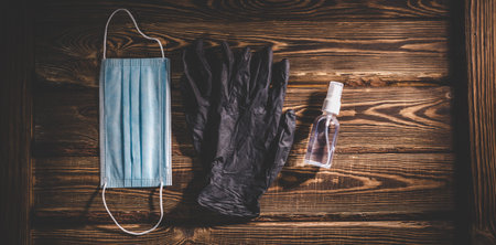 Medical mask, black rubber gloves and a transparent sanitizer on a wooden background. Covid-19 virus protection medical concept. Studio photo with vignetting.の写真素材