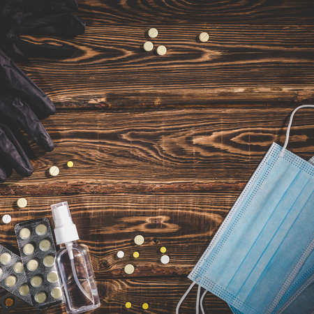 Medical masks, pills, antiseptic in a transparent plastic bottle and black rubber gloves on a wooden background. Covid-19 virus protection medical concept. Studio photo with vignetting.の写真素材
