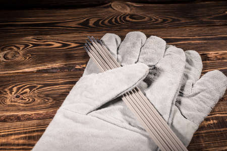 White leather welding glove and welding electrodes on a wooden background. Studio photo in hard light.の写真素材