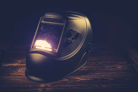 Black welding mask on a wooden background. A studio photo with hard lighting.の写真素材