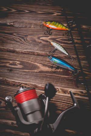 Studio photo of fishing tackle on a wooden background. A rod, a reel with a line and three wobblers. Photo with vignettingの写真素材