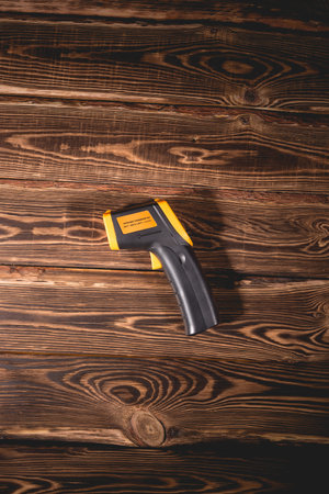 Yellow-black pyrometer on a wooden background. A device for non-contact temperature measurement. Studio photo.の写真素材
