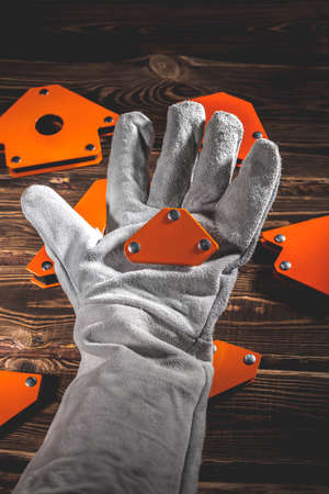 A man's hand holds a magnetic angle for welding metal constructions with a fixed angle value. Studio photo with hard lighting on a wooden backgroundの写真素材