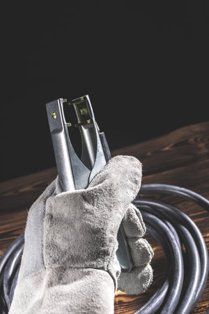 A welder in white welding gloves holds a wire with a ground terminal in his hand. Studio photo in...