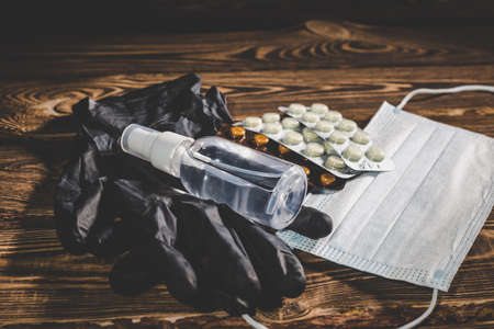 Medical mask, pills, antiseptic in a transparent plastic bottle and black rubber gloves on a wooden background. virus protection medical concept. Studio photo with vignetting.の写真素材