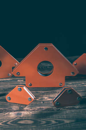 A set of orange magnetic corners for welding metal structures with a fixed angle value. Studio photo with hard lighting on a wooden background.の写真素材