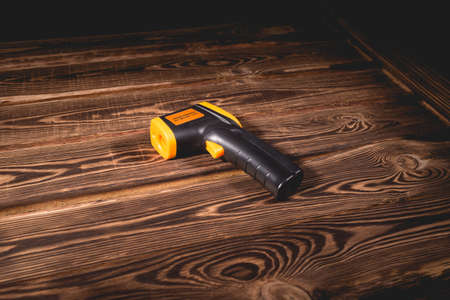 Yellow-black pyrometer on a wooden background. A device for non-contact temperature measurement. Studio photo.の写真素材