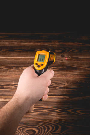 A man holds a yellow-black pyrometer on a wooden background. A device for non-contact temperature measurement. Studio photo.の写真素材