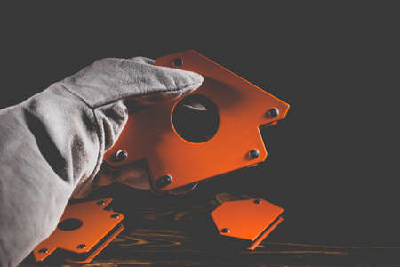 A man's hand holds a magnetic angle for welding metal constructions with a fixed angle value. Studio photo with hard lighting on a wooden backgroundの写真素材