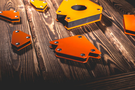 A set of orange magnetic corners for welding metal structures with a fixed angle value. Studio photo with hard lighting on a wooden background.の写真素材