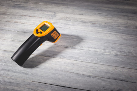 Yellow-black pyrometer on a wooden background. A device for non-contact temperature measurement....