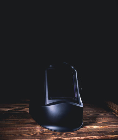 Black welding mask on a wooden background. A studio photo with hard lighting.