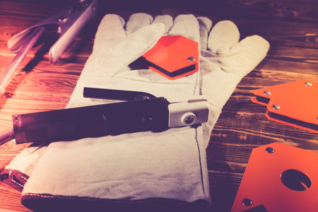 Welding wires, electrode holder and earth terminal, white leather welding gloves, magnetic welding corners on a wooden background. Studio photo in hard light.の写真素材