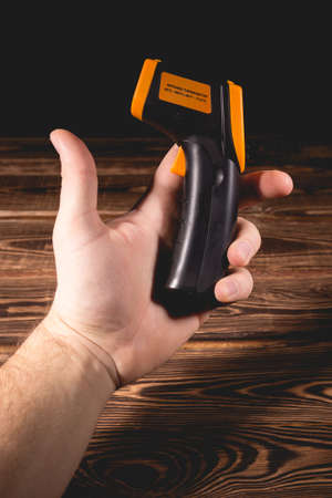 A man holds a yellow-black pyrometer on a wooden background. A device for non-contact temperature measurement. Studio photo.の写真素材