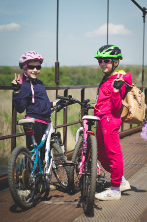 Konstantinovka, Ukraine - May 8, 2021: Two little cute girls in helmets with bicycles on the old iron bridge show the sign "Peace".のeditorial素材