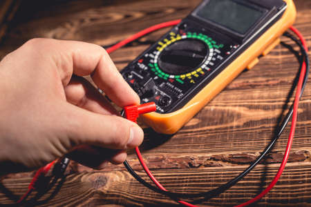 Multimeter and two test leads on a wooden background. A man's hand holds two test leads. A studio photo with hard lighting.の写真素材