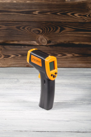 Yellow-black pyrometer on a wooden background. A device for non-contact temperature measurement....