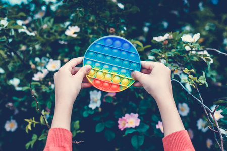 A little cute girl is holding a bright, colorful anti-stress toy pop it.の写真素材