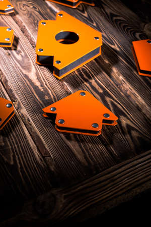 A set of orange magnetic corners for welding metal structures with a fixed angle value. Studio photo with hard lighting on a wooden background.の写真素材
