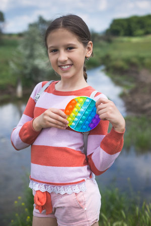 Little cute girl posing in nature with a pop-it antistress toy in her hands.の写真素材
