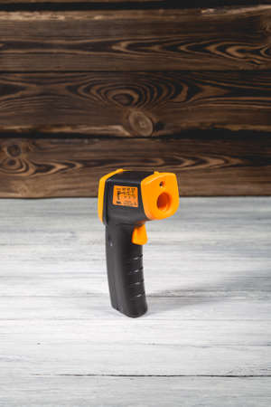 Yellow-black pyrometer on a wooden background. A device for non-contact temperature measurement. Studio photo.の写真素材