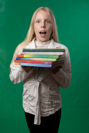 Little cute schoolgirl posing on a green background. Studio photo of a school theme.の写真素材