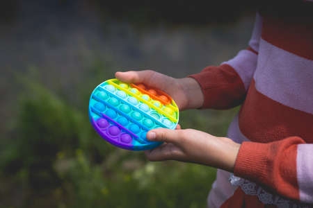 Little cute girl posing in nature with a pop-it antistress toy in her hands.の写真素材