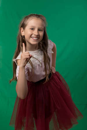 Little cute schoolgirl posing on a green background. Studio photo of a school theme.の写真素材
