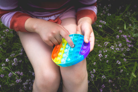 A little cute girl is sitting on the grass with a - antistress toy.の写真素材