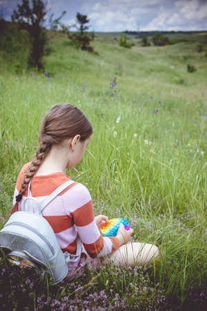 A little cute girl is sitting on the grass with a pop it - antistress toy.の写真素材