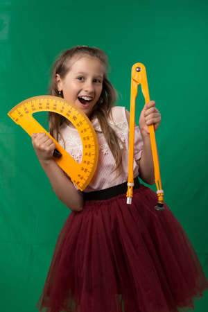 Little cute schoolgirl posing on a green background. Studio photo of a school theme.の写真素材
