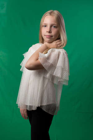 Little cute schoolgirl posing on a green background. Studio photo of a school theme.の写真素材