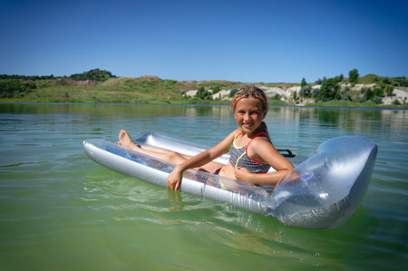 A little cute girl in a swimsuit swims on an inflatable mattress on a blue career lake.の写真素材
