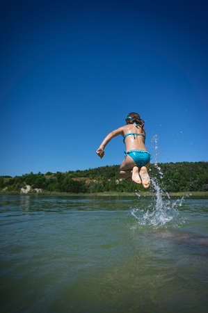 A little cute girl in a swimsuit jumps into the blue water of a career lake.の写真素材