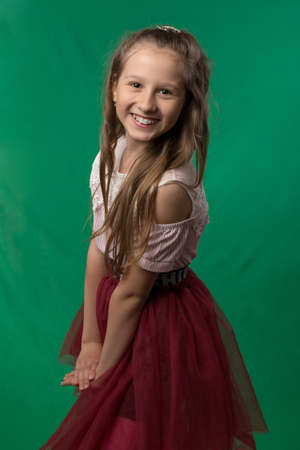 Little cute schoolgirl posing on a green background. Studio photo of a school theme.の写真素材