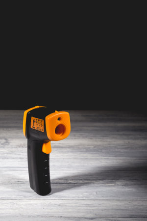 Yellow-black pyrometer on a wooden background. A device for non-contact temperature measurement. Studio photo.の写真素材