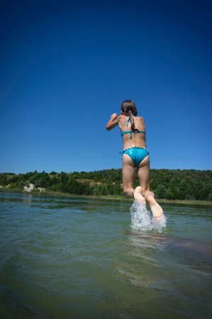 A little cute girl in a swimsuit jumps into the blue water of a career lake.の写真素材