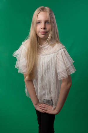 Little cute schoolgirl posing on a green background. Studio photo of a school theme.の写真素材