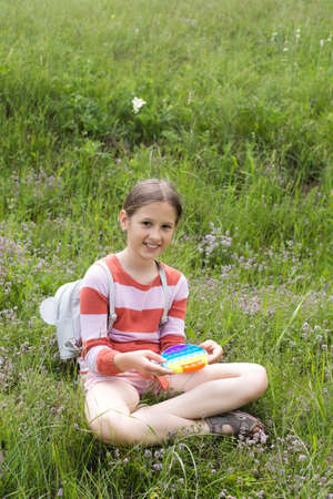 A little cute girl is sitting on the grass with a pop it - antistress toy.の写真素材