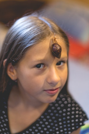 Little Achatina snail on the forehead of a cute little girlの写真素材