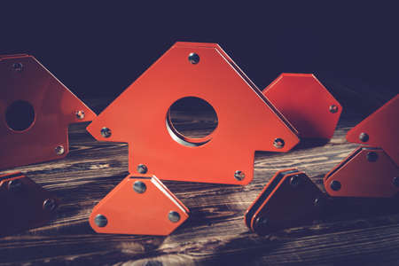 A set of orange magnetic corners for welding metal structures with a fixed angle value. Studio photo with hard lighting on a wooden background.の写真素材